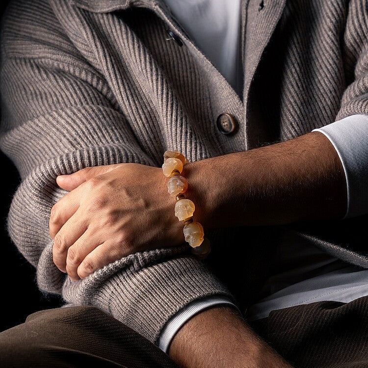 Man wearing a gray cardigan and a bracelet with beige beads.