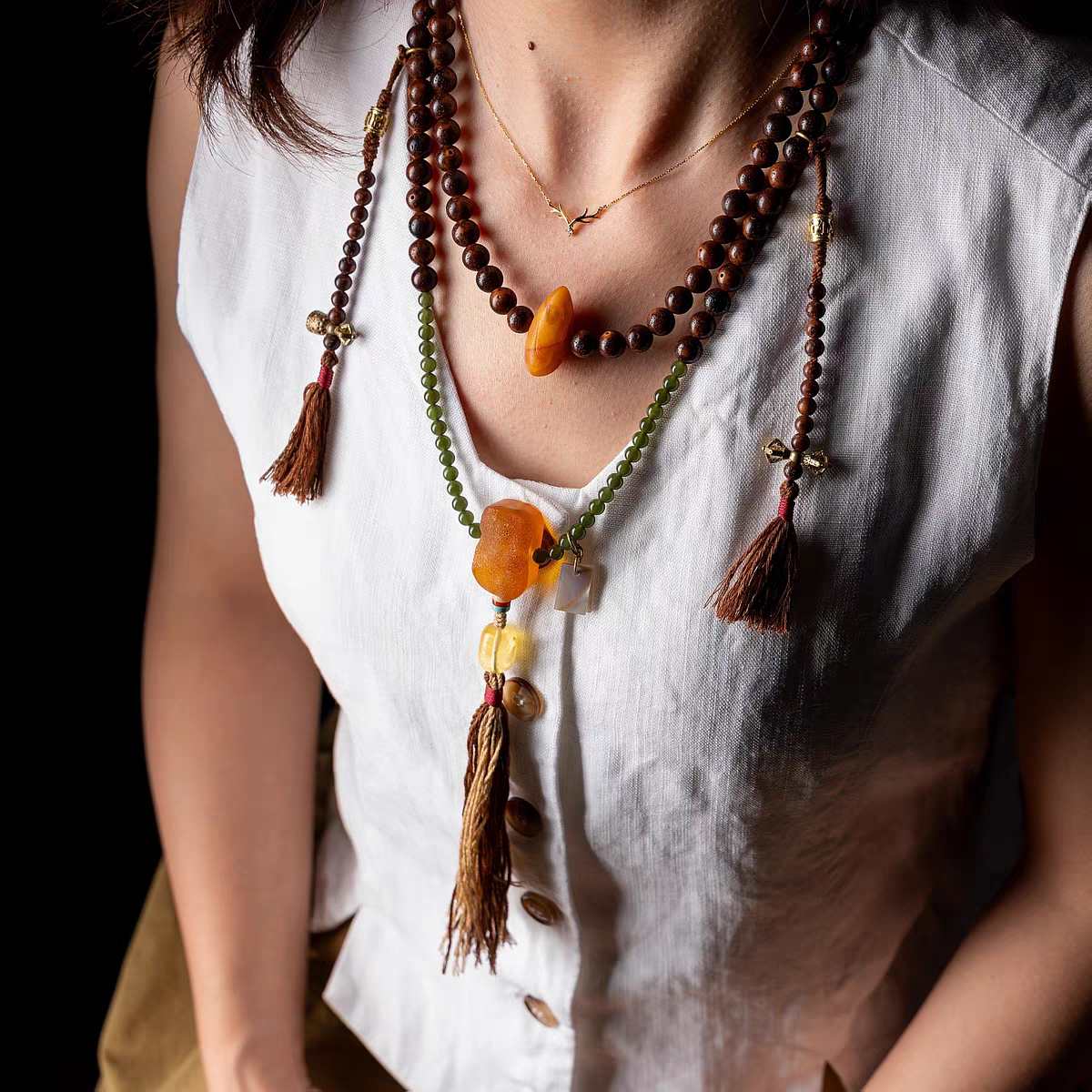 Close-up of a person wearing a long beaded necklace with tassels on a white shirt.