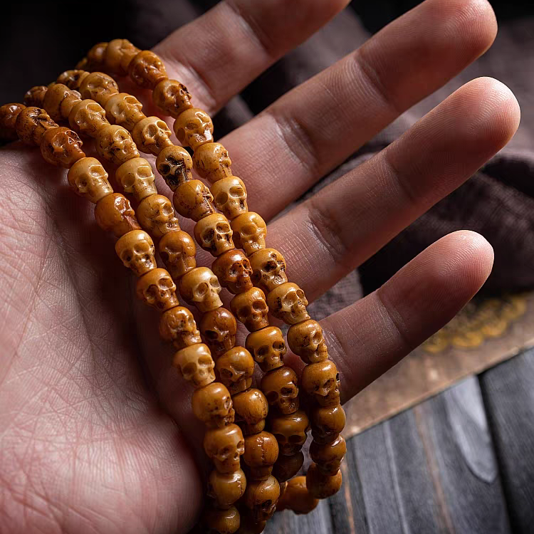 Hand holding a stack of brown beaded bracelets on a wooden surface