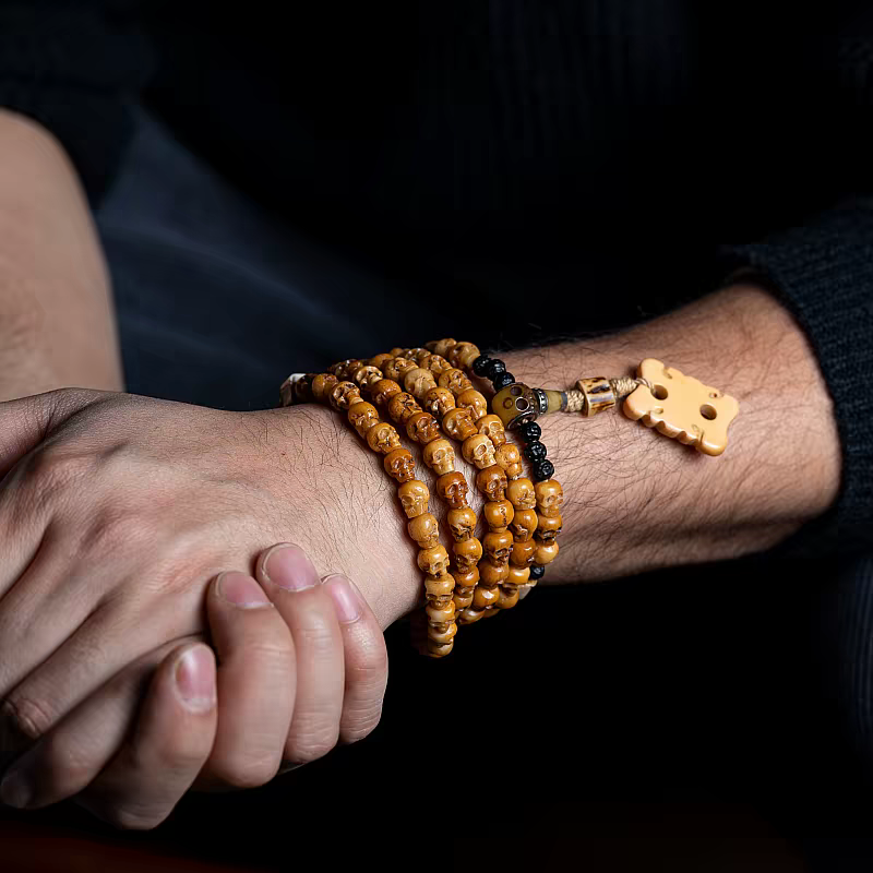 Two hands shaking with a person wearing multiple wooden beaded bracelets on a dark background