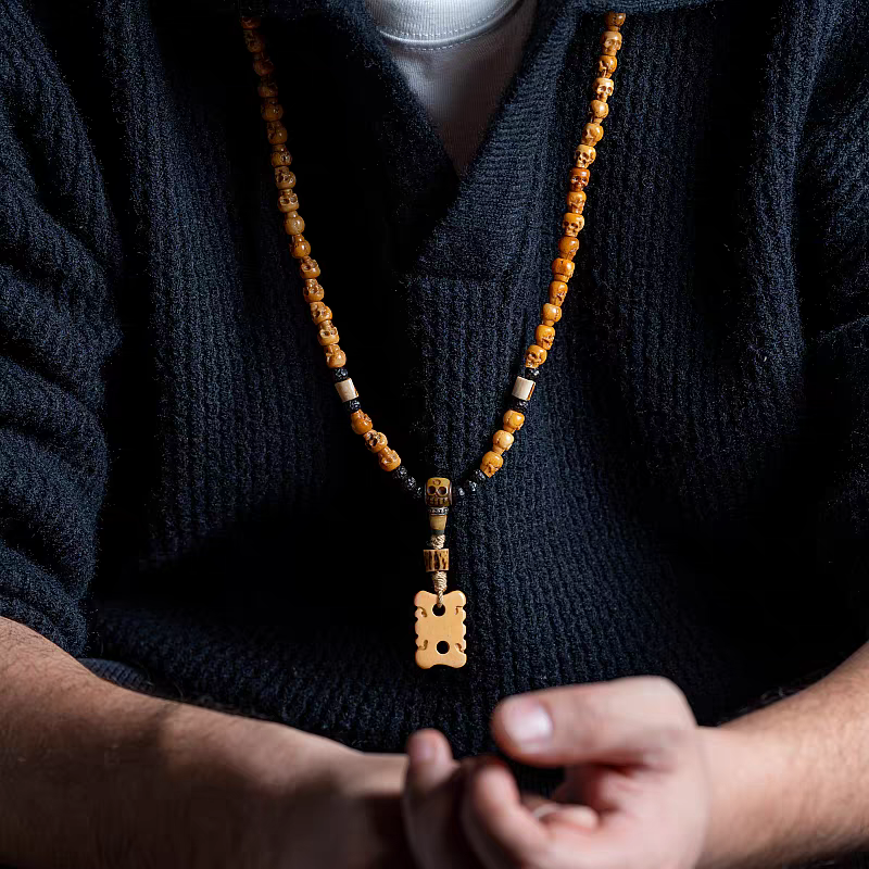 Person wearing a dark sweater with a beaded necklace featuring a large pendant.