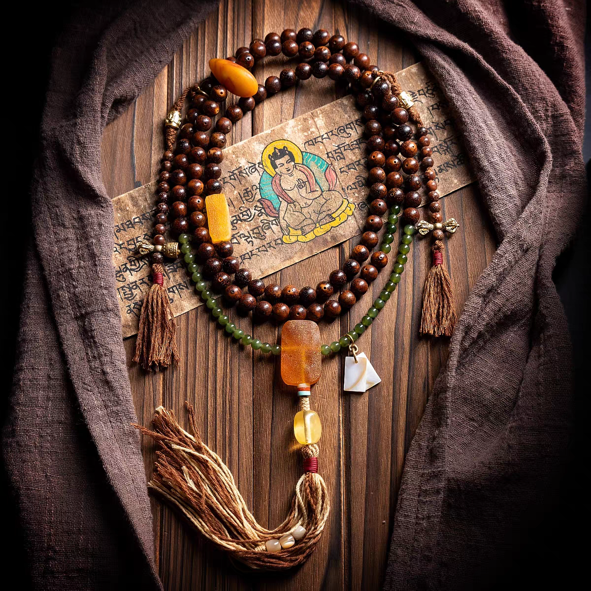 Wooden beaded necklace with tassels on a wooden surface with a cloth and a small painting.