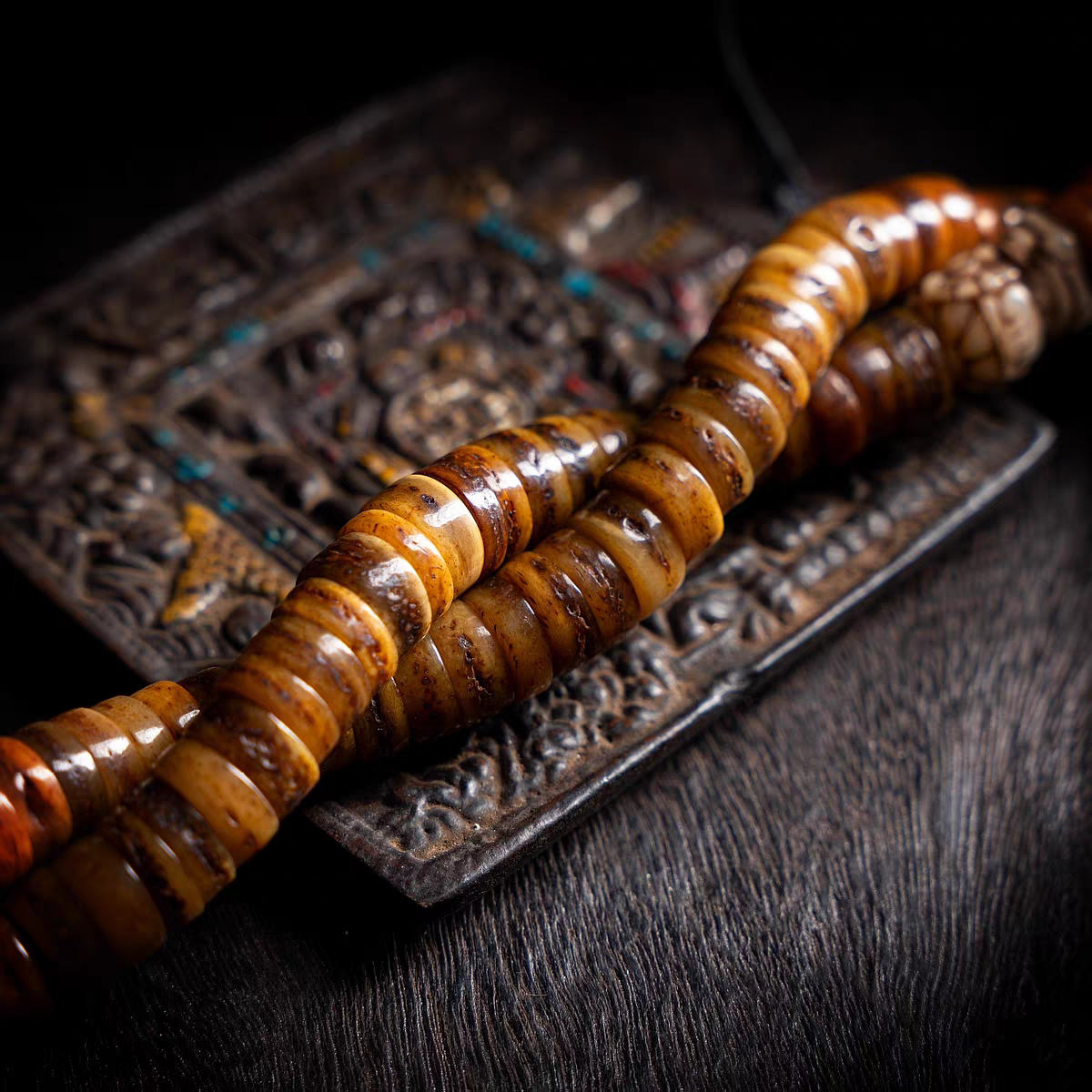 Brown beaded mala on an ornate metal plate with a dark background